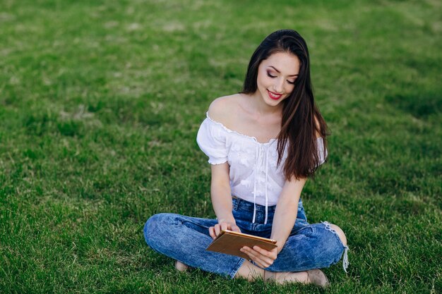 Jong meisje zitten in een park te kijken met een glimlach een tablet