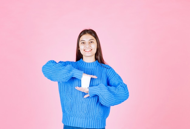 jong meisjesmodel dat een plastic kop op roze muur houdt.