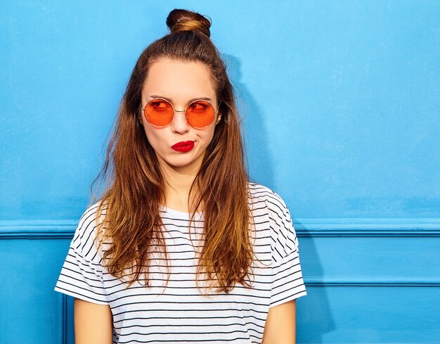 Jong modieus vrouwenmodel in toevallige de zomerkleren met rode lippen, die dichtbij blauwe muur stellen