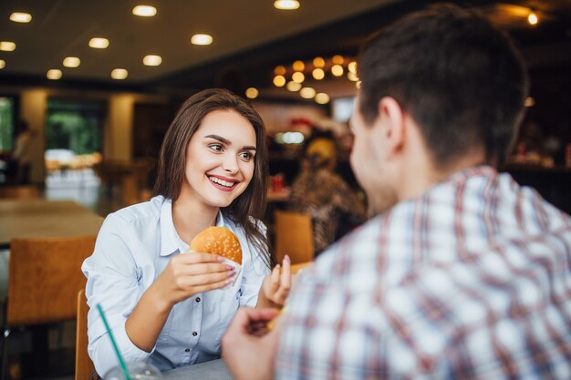 Jong, mooi donkerbruin meisje tijdens de lunch in een fastfoodrestaurant met een jonge jongen die hamburgers en frietjes eet