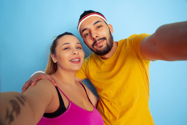 Jong mooi Kaukasisch paar in lichte kleren opleiding op blauwe achtergrond Concept van sport, menselijke emoties, meningsuiting, gezonde levensstijl, relatie, familie. Samen selfie maken en knuffelen.