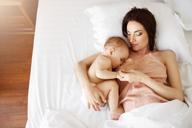 Jong mooi mamma die haar pasgeboren baby de borst geven liggend in bed thuis. Van boven.