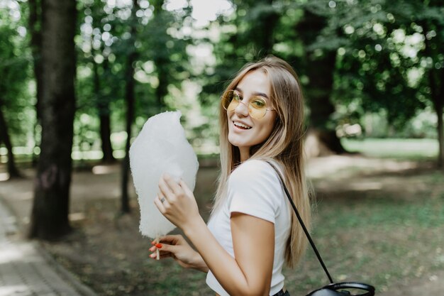 Jong mooi meisje dat gesponnen suiker in het park eet