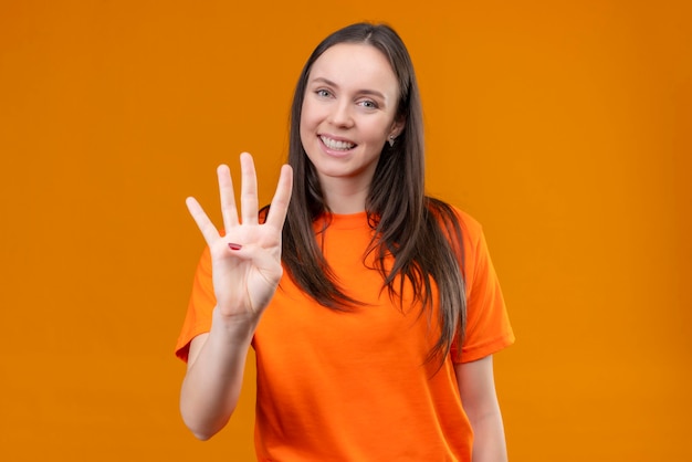 Jong mooi meisje dat oranje t-shirt draagt dat en met vingers nummer vier toont die zich over geïsoleerde oranje achtergrond bevinden