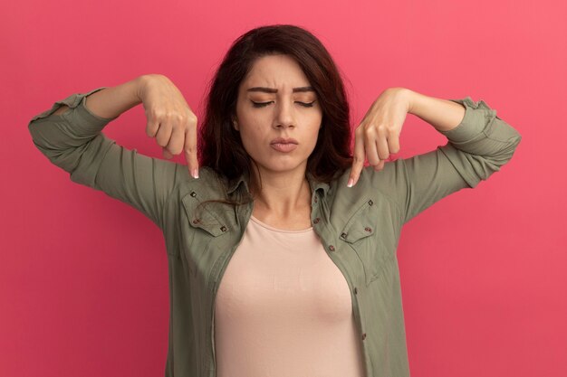 Jong mooi meisje met gesloten ogen die olijfgroene t-shirtpunten dragen op neer geïsoleerd op roze muur