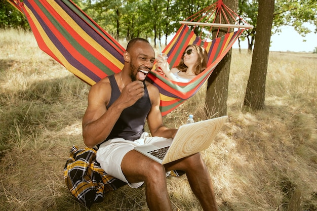 Jong multi-etnisch internationaal romantisch koppel buiten op de weide in zonnige zomerdag. afro-amerikaanse man en blanke vrouw met picknick samen. concept van relatie, zomer.