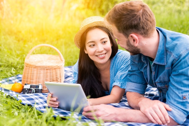 Jong paar dat bij elkaar glimlacht terwijl het houden van tablet op picknick