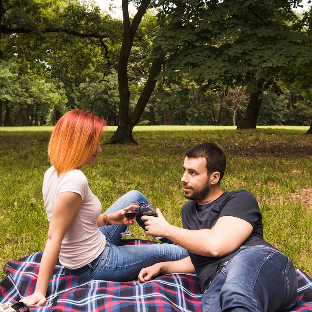 Gratis foto jong paar die wijnglazen roosteren op deken over het groene gras