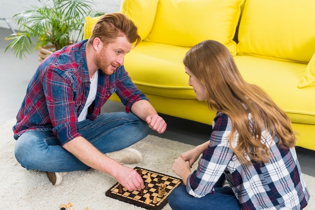 Gratis foto jong paar twee die het schaak in de woonkamer spelen