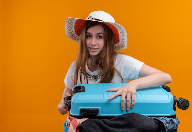 Jong reizigersmeisje die de koffer van de hoedenholding met doeken dragen die op geïsoleerde oranje muur met exemplaarruimte kijken