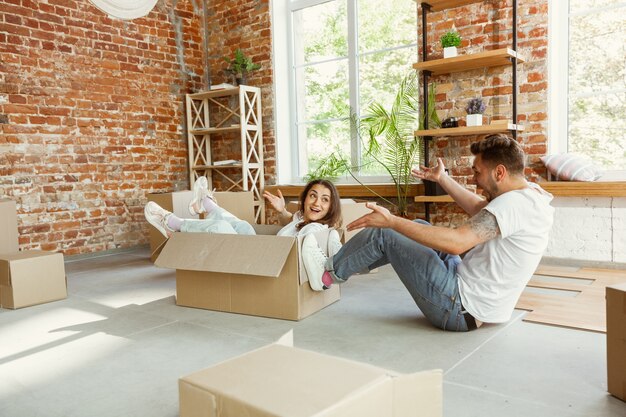 Jong stel verhuisde naar een nieuw huis of appartement. Plezier hebben met kartonnen dozen, ontspannen na het schoonmaken en uitpakken op een verhuisdag. Kijk gelukkig. Familie, verhuizen, relaties, eerste huisconcept.