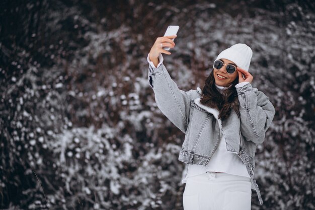 Jong trendy meisje in een de winterpark die telefoon met behulp van