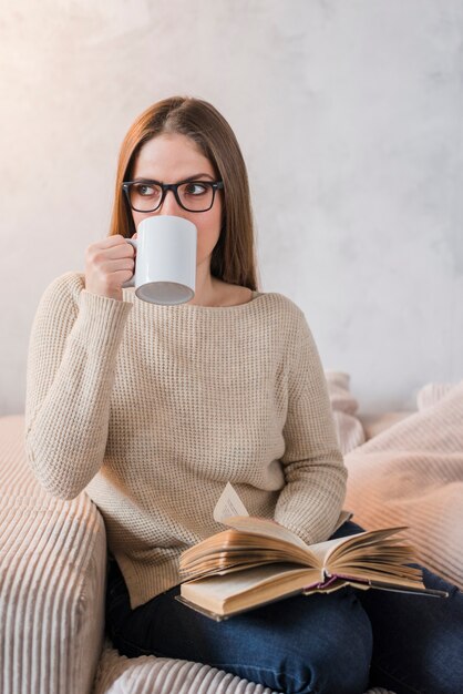 Jong vrouw het drinken boek van de koffieholding in hand