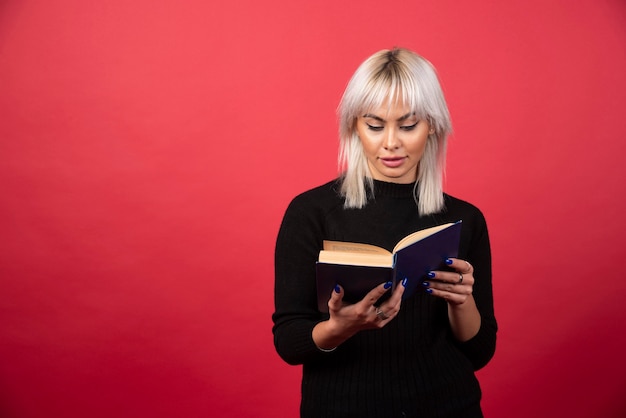 Jong vrouwenmodel dat een boek op een rode achtergrond leest. Hoge kwaliteit foto