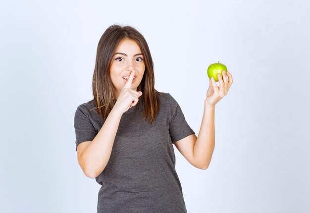 jong vrouwenmodel dat een groene appel houdt en stil teken doet.