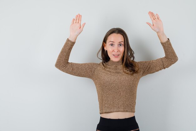 Jong wijfje dat haar handen met open handpalmen in gouden blouse vooraanzicht opheft.