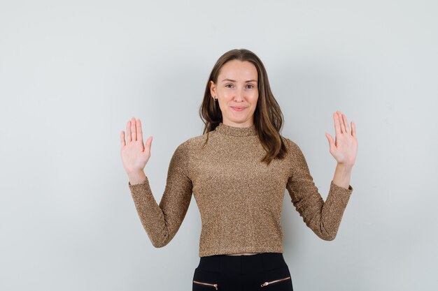 Jong wijfje dat haar handen opheft terwijl zij haar handpalmen in gouden blouse toont en kalm kijkt. vooraanzicht.