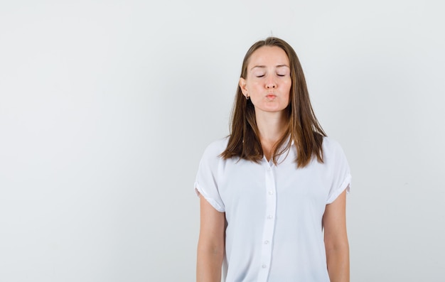 Jong wijfje dat haar ogen sluit terwijl zij in witte blouse staat en stil kijkt