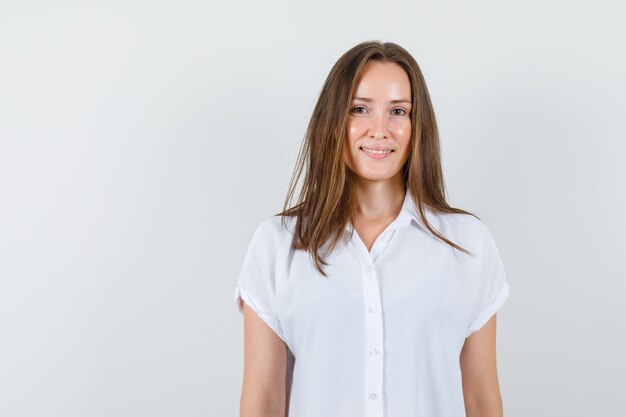 Jong wijfje dat in witte blouse glimlacht en leuk kijkt