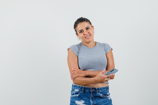 Jong wijfje dat mobiele telefoon in t-shirt, korte broek houdt en vrolijk kijkt.