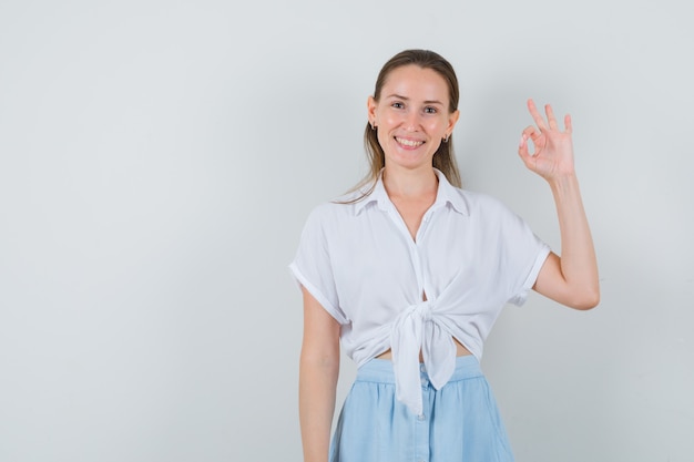 Jong wijfje dat ok gebaar in blouse en rok toont en joviaal kijkt