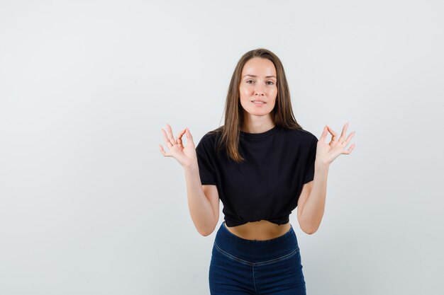 Jong wijfje dat ok teken in zwarte blouse, broek toont en zelfverzekerd kijkt