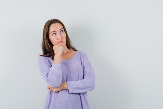 Jong wijfje dat opzij in lila blouse kijkt en nadenkend kijkt. vooraanzicht.