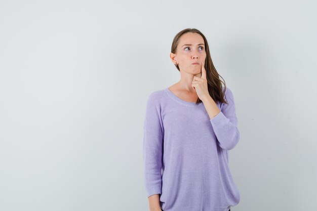 Jong wijfje dat weg in lila blouse kijkt en nadenkend kijkt. vooraanzicht.