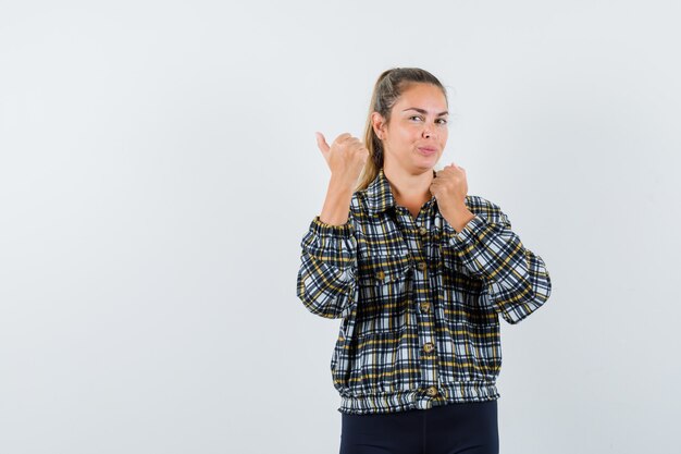 Jong wijfje dat weg met duim in overhemd, korte broek wijst en er zelfverzekerd uitziet. vooraanzicht.