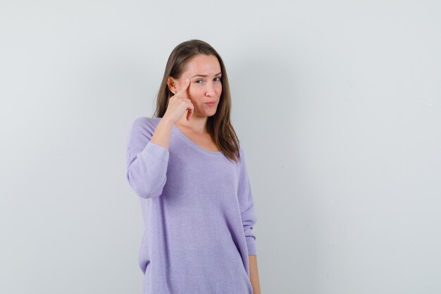 Jong wijfje in lila blouse die op haar tempel richt en geconcentreerd kijkt