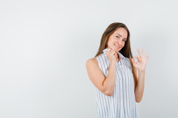 Jong wijfje in t-shirt die ok teken tonen terwijl kraag vasthoudt en er vrolijk, vooraanzicht uitziet.