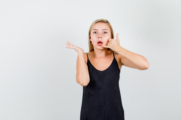 Jong wijfje in zwart hemd dat telefoongesprekgebaar toont en ernstig kijkt