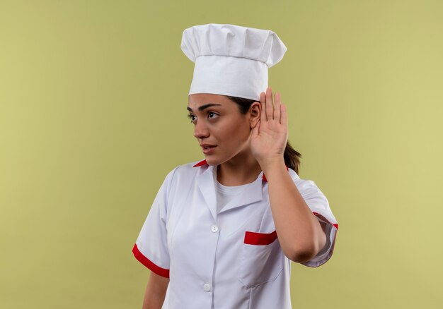 Jong zelfverzekerd Kaukasisch kokmeisje in chef-kok uniforme gebaren kan geen teken horen dat op groene muur met exemplaarruimte wordt geïsoleerd