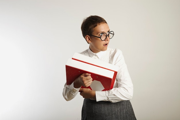 Jonge aantrekkelijke Europese leraar in witte blouse en grijze rok die rode en witte bindmiddelen houdt rolt ogen in ongeloof op witte muur