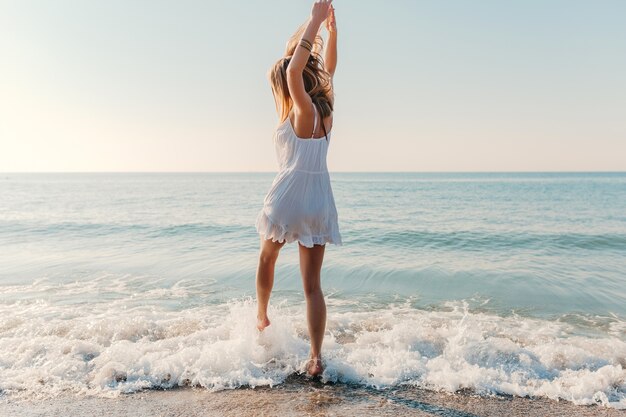 Jonge aantrekkelijke gelukkige vrouw dansen ronddraaien door zee strand zonnige zomer mode-stijl in witte jurk vakantie