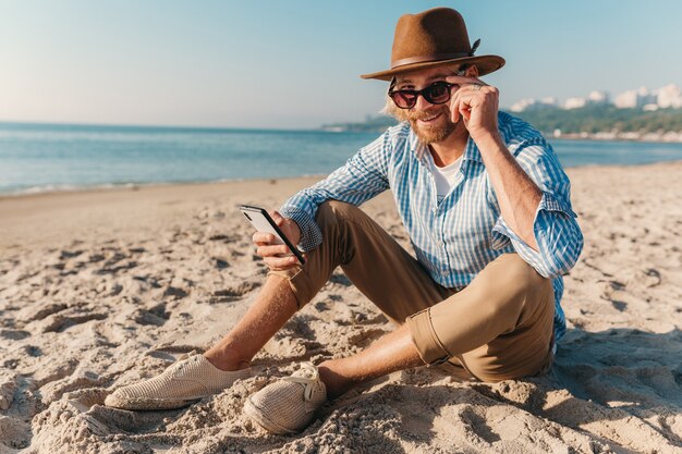Jonge aantrekkelijke hipster man zittend op het strand aan zee op zomervakantie