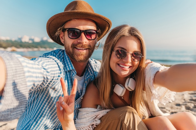 Jonge aantrekkelijke lachende gelukkig man en vrouw in zonnebril zittend op zand strand selfie foto te nemen