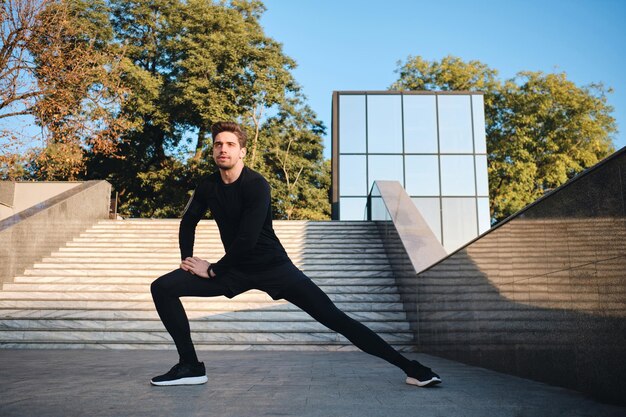 Jonge aantrekkelijke sportieve man die zich uitstrekt tijdens de ochtendtraining in het stadspark