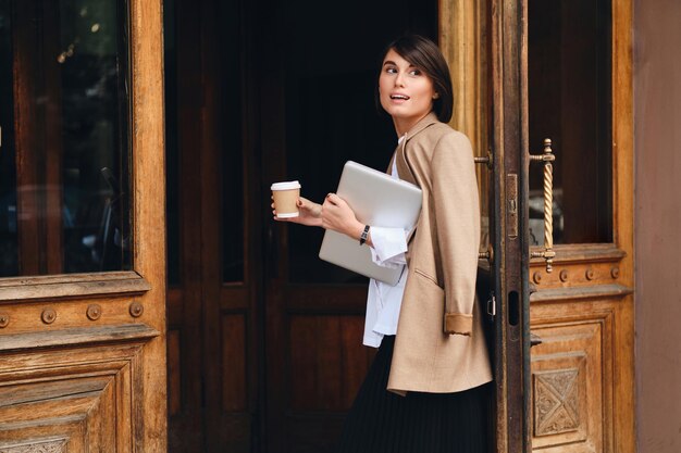 Jonge aantrekkelijke stijlvolle zakenvrouw met laptop en koffie om naar buiten te gaan