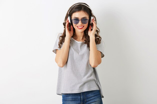 Jonge aantrekkelijke vrouw die aan muziek op hoofdtelefoons luistert, die zonnebril draagt, die op witte achtergrond wordt geïsoleerd,