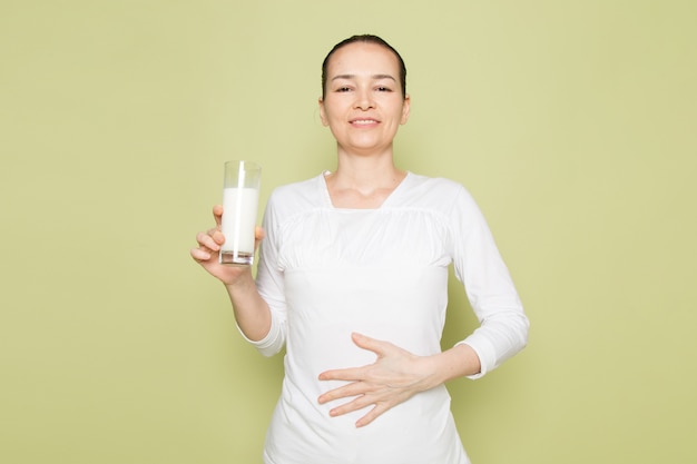 Jonge aantrekkelijke vrouw in wit overhemd die en glas met melk glimlachen houden