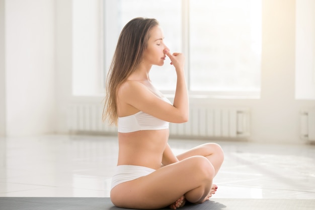 Jonge aantrekkelijke vrouw maken alternatieve neusgat ademhaling, wit
