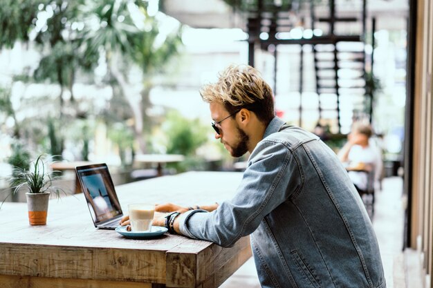 Gratis foto jonge aantrekkelijke zakenman in een café werkt voor een laptop, drinkt koffie.