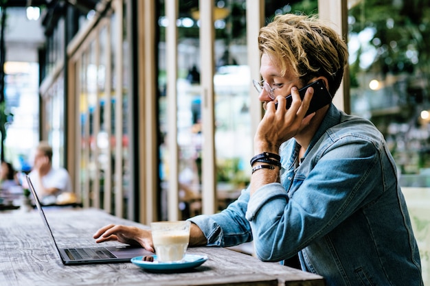 Gratis foto jonge aantrekkelijke zakenman in een café werkt voor een laptop, drinkt koffie.