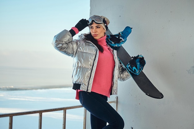 Jonge actieve vrouw met snowboard poseert voor fotograaf op heldere winterdag.