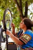 Gratis foto jonge actieve vrouwelijke fietser die een moersleutel grijpt om schroeven aan te halen en fietsonderdelen buiten te onderhouden. sportieve enthousiaste afro-amerikaanse vrouw met professioneel hulpmiddel voor fietsonderhoud in ho