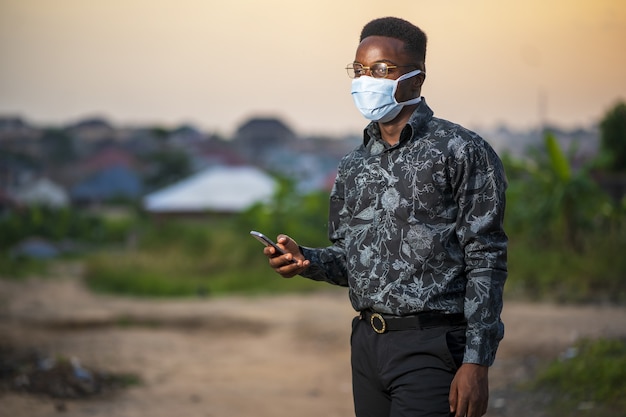 Jonge African American man draagt een beschermend gezichtsmasker met zijn telefoon buitenshuis