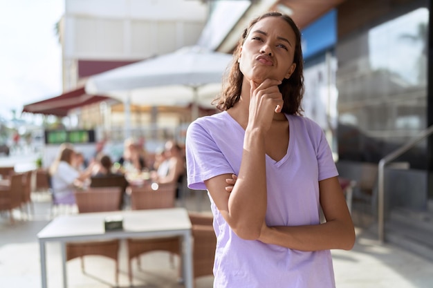 Jonge afrikaanse amerikaanse vrouw die zich met twijfeluitdrukking bij het terras van de koffiewinkel bevindt