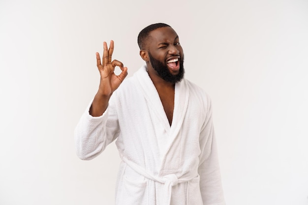 Jonge Afrikaanse man in badjas bereidt zich voor op huidverzorging met ok vingerteken Menselijke emoties concept