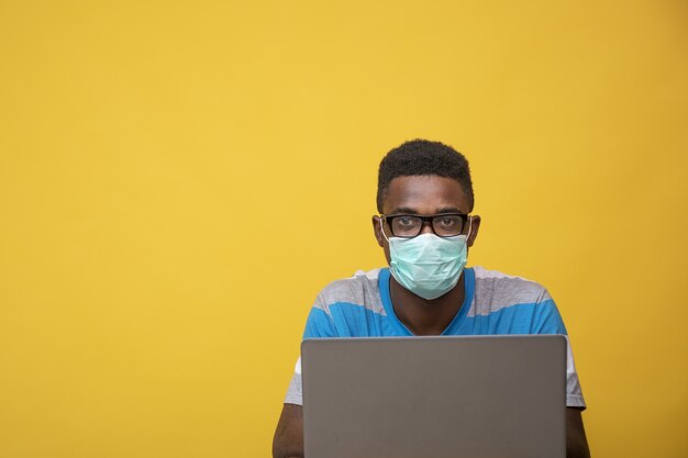 Jonge afrikaanse man met een bril en een gezichtsmasker terwijl hij op zijn laptop werkt - covid-19